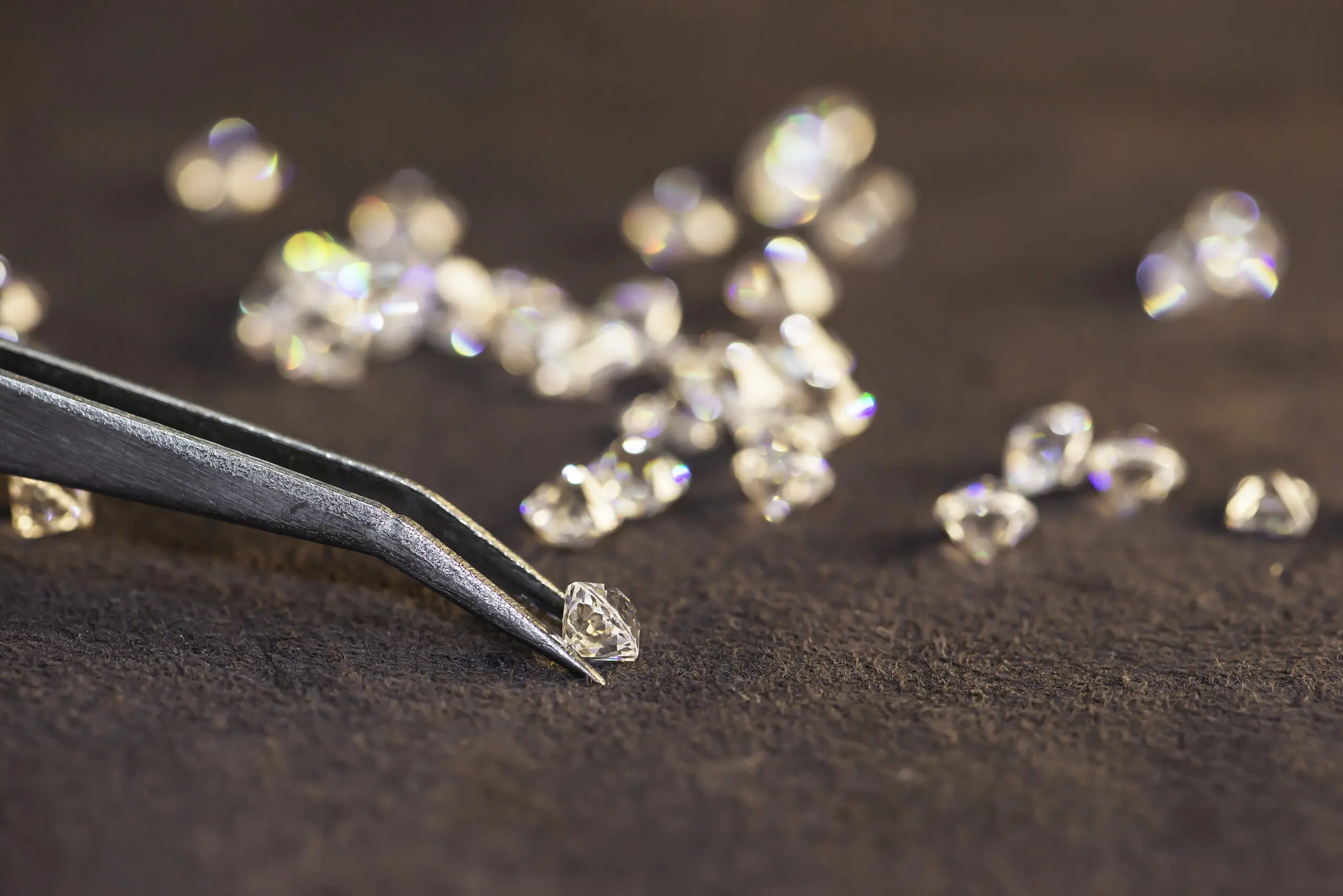 Tweezers holding small diamond, scattered diamonds nearby.
